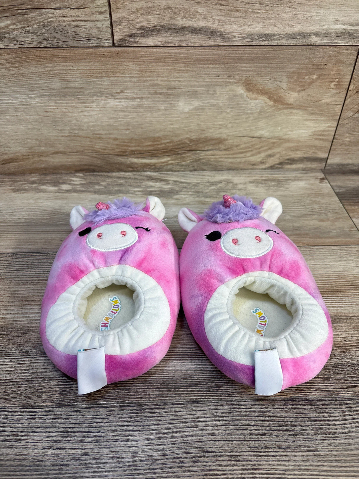 Pink unicorn plush slippers for kids with purple mane and horn on wooden floor