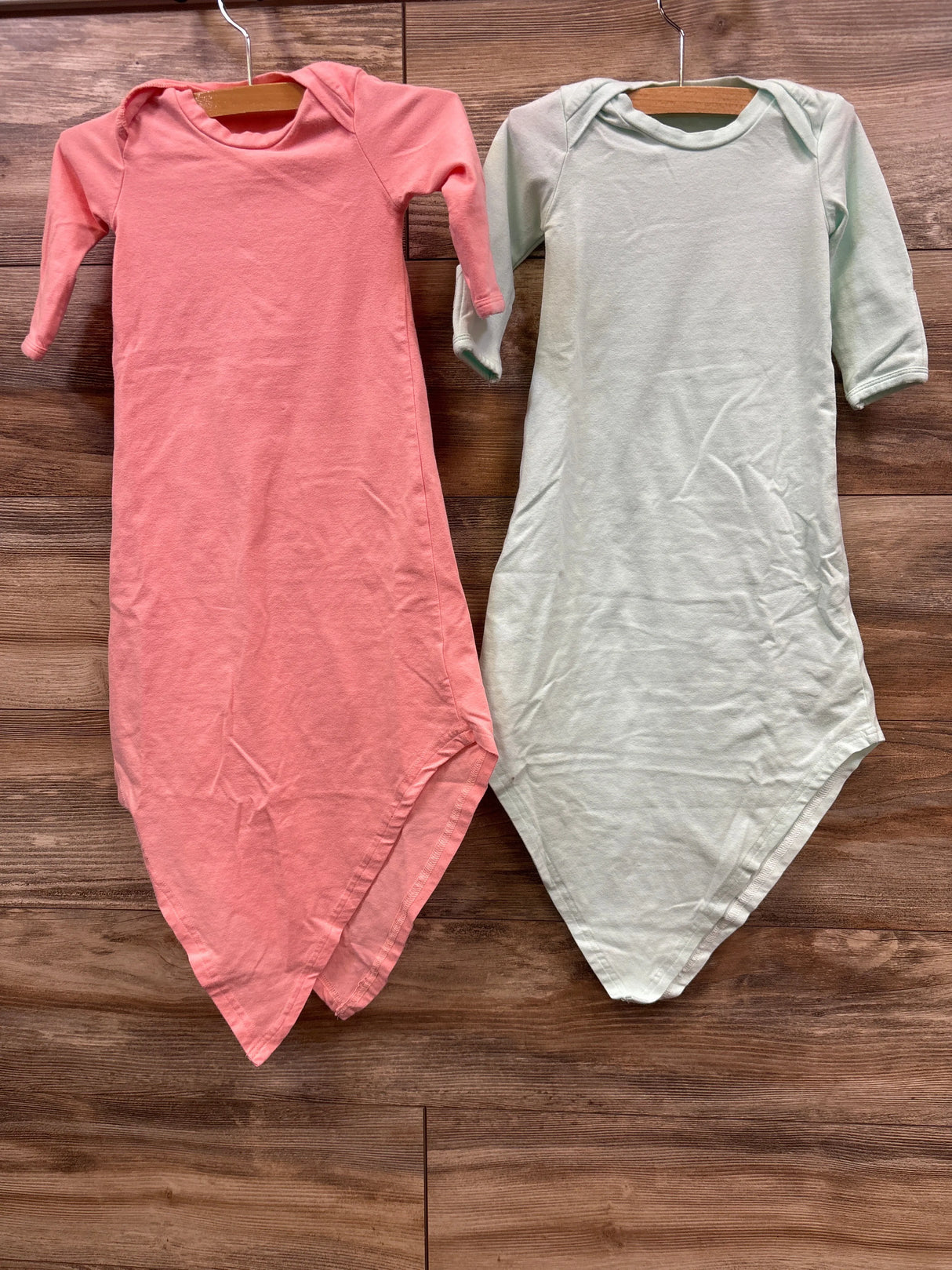 Pink and light green long sleeve baby gowns hanging on wooden hangers over wood floor