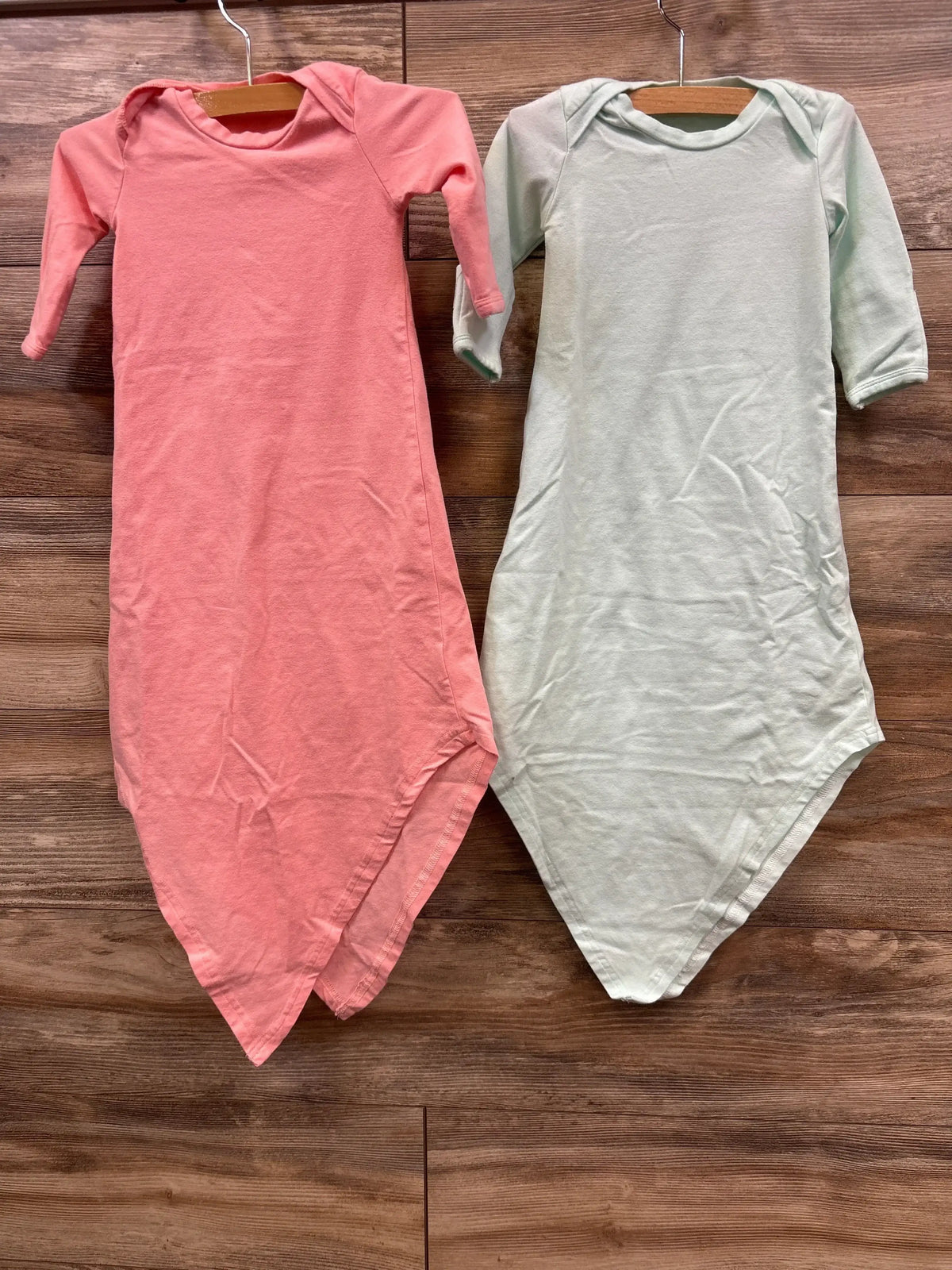 Flat lay of Baby Noah 2pk knotted gown set size 3m showcasing pink and mint green long sleeve gowns on wooden hangers over wood plank floor