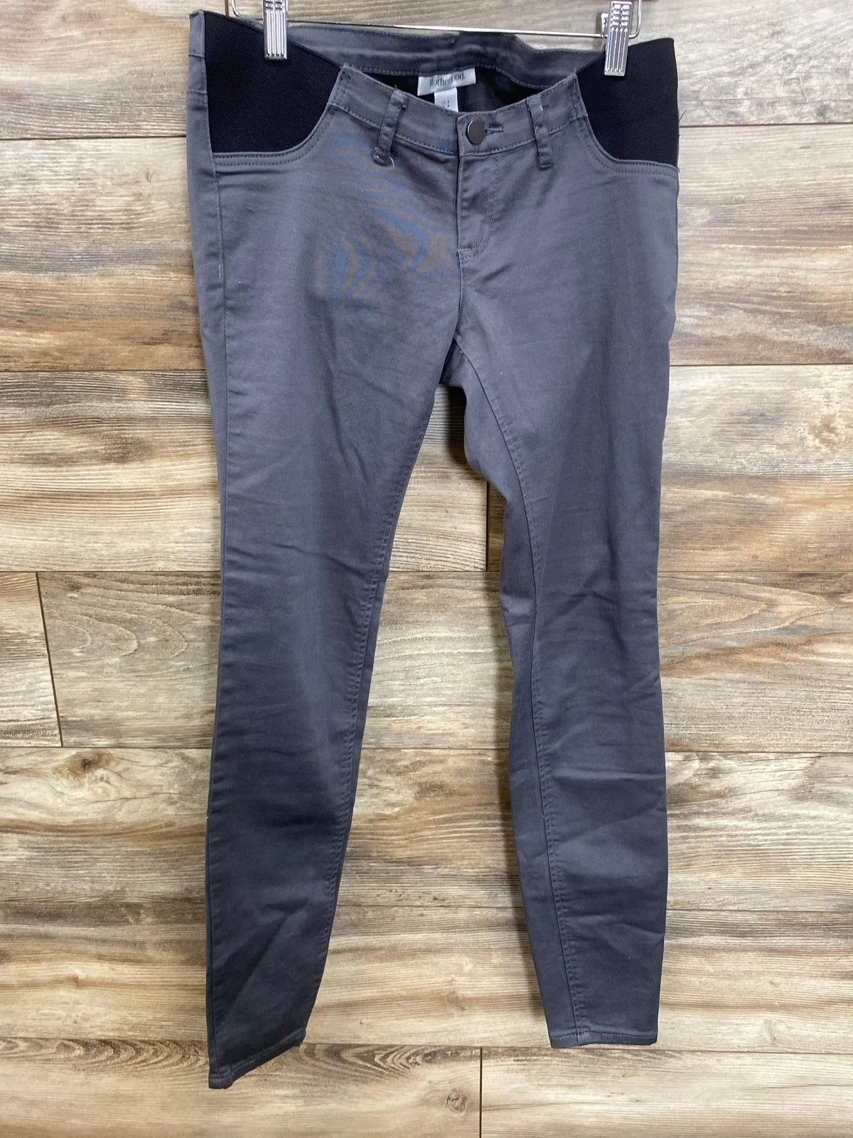 Gray maternity pants with black belly panel, hanging on hanger against wood background