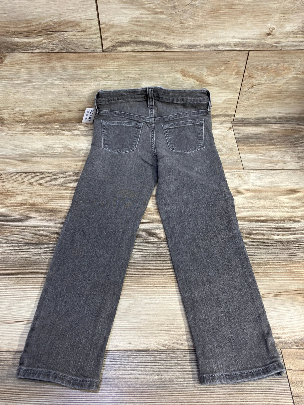 Gray kids jeans with back pockets displayed on wooden floor, gently used children's denim pants