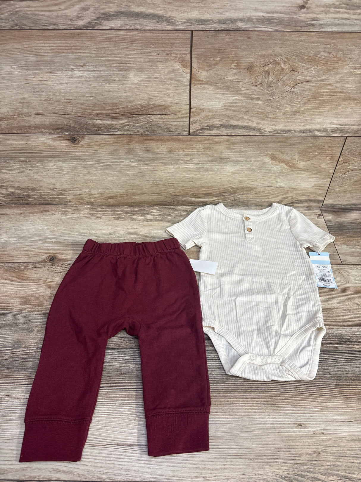 White short-sleeve baby bodysuit with buttons paired with maroon elastic waist pants on wooden floor