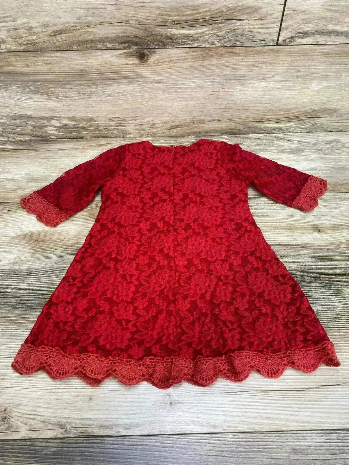 Flat lay of April Girl red toddler lace dress (back) showing 3/4 sleeves, floral lace and scalloped hem on wood background