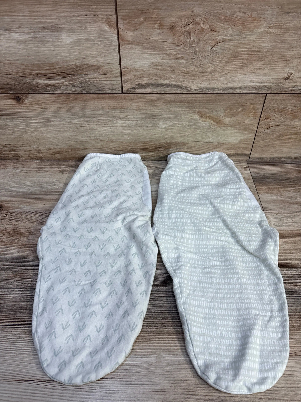 Top view of KeaBabies Soothe Swaddle Wrap two-pack showcasing leaf and striped patterns on a wood-look floor
