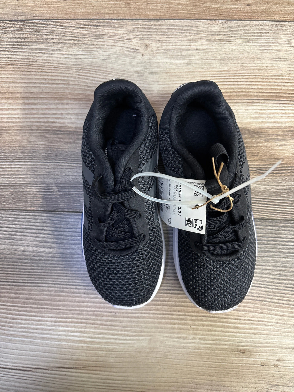 Top-down of Adidas Racer TR 2.01 toddler sneakers showing black knit upper and white soles on light wood background