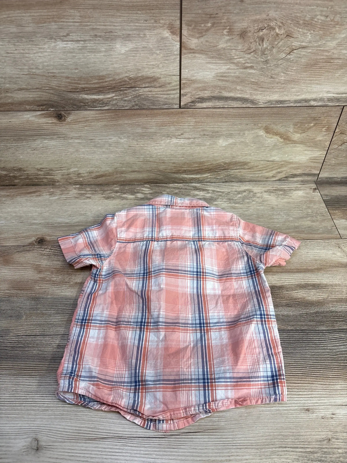 Back view of Oshkosh short-sleeve plaid button-up shirt in coral pink and navy showing yoke seam and curved hem on wood floor