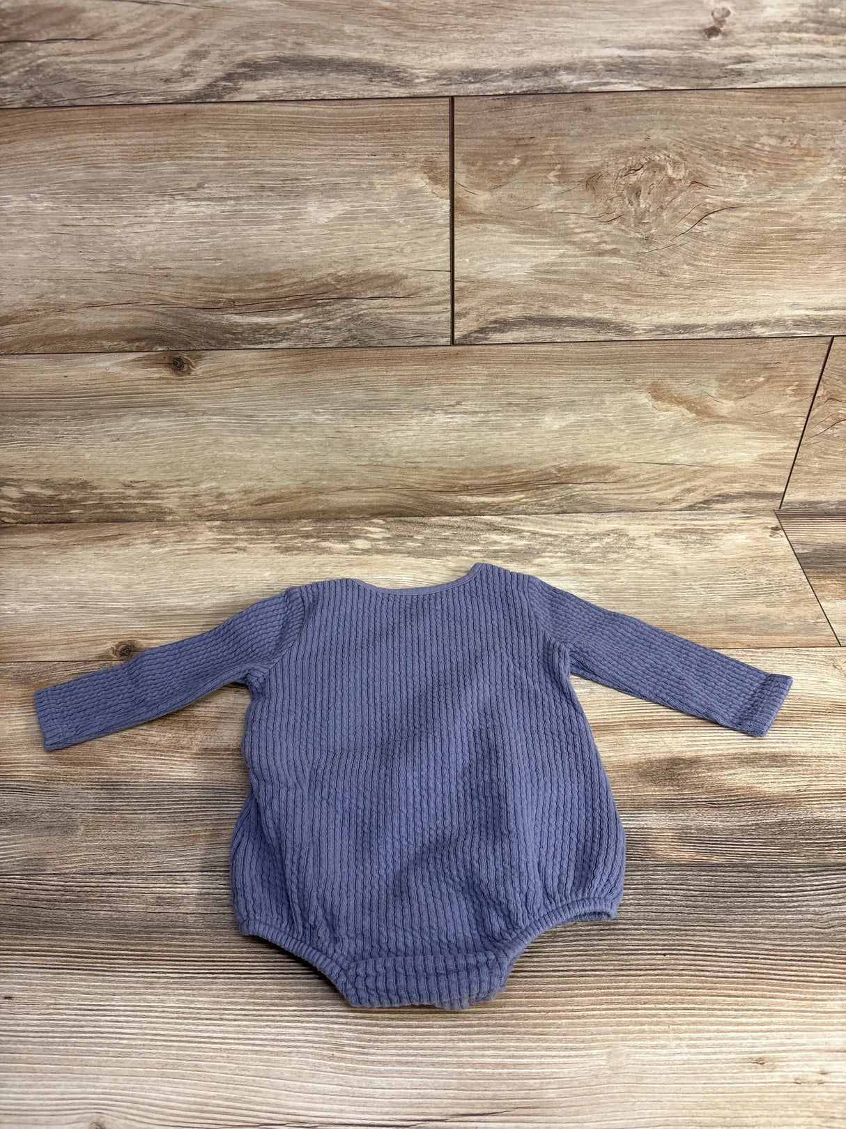 Long sleeve purple textured baby onesie laid flat on wooden floor background