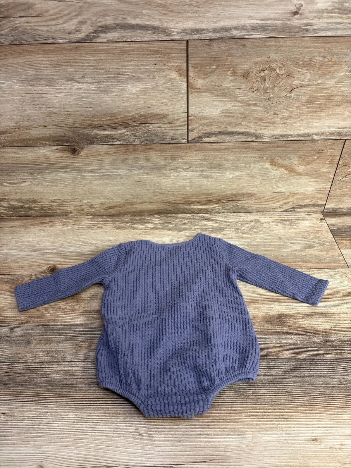 Long sleeve purple textured baby onesie laid flat on wooden floor background