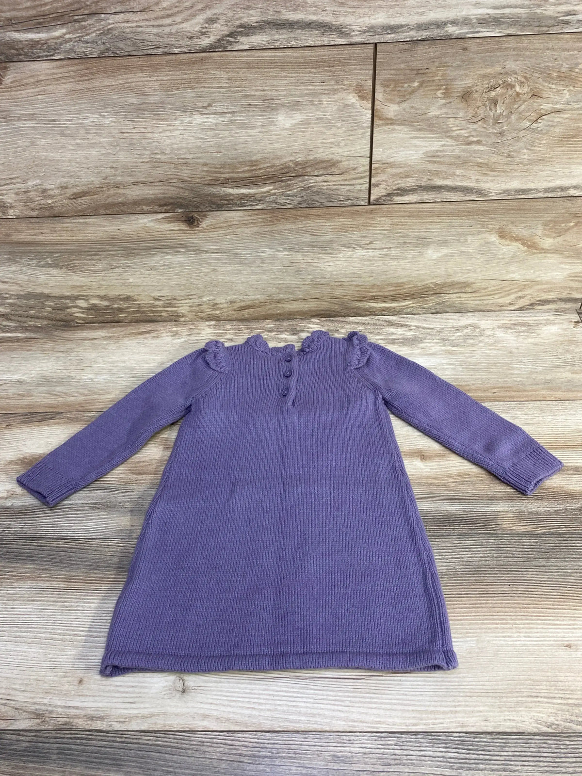 Purple knit long-sleeve baby dress with ruffled collar and button details on wood floor