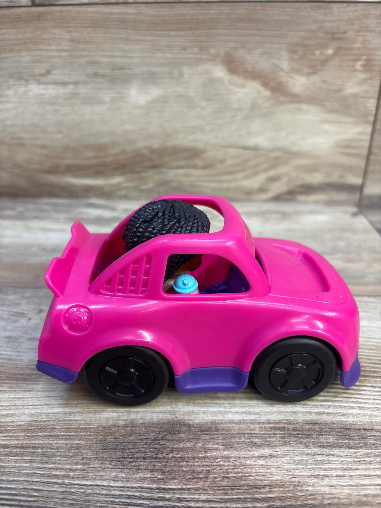 Side view of Fisher-Price Little People Barbie pink convertible with seated figure holding a blue sippy cup on a wood surface
