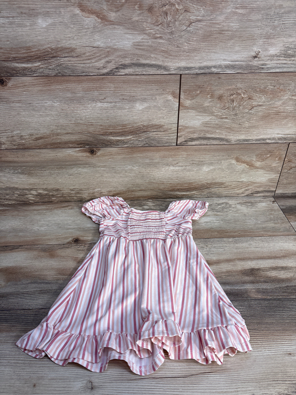 Pink and white striped baby dress with ruffled hem and short puff sleeves on wood floor