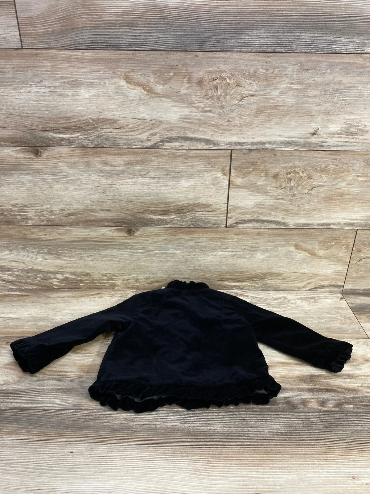 Black velvet long sleeve baby jacket with ruffled cuffs and hem on wooden floor