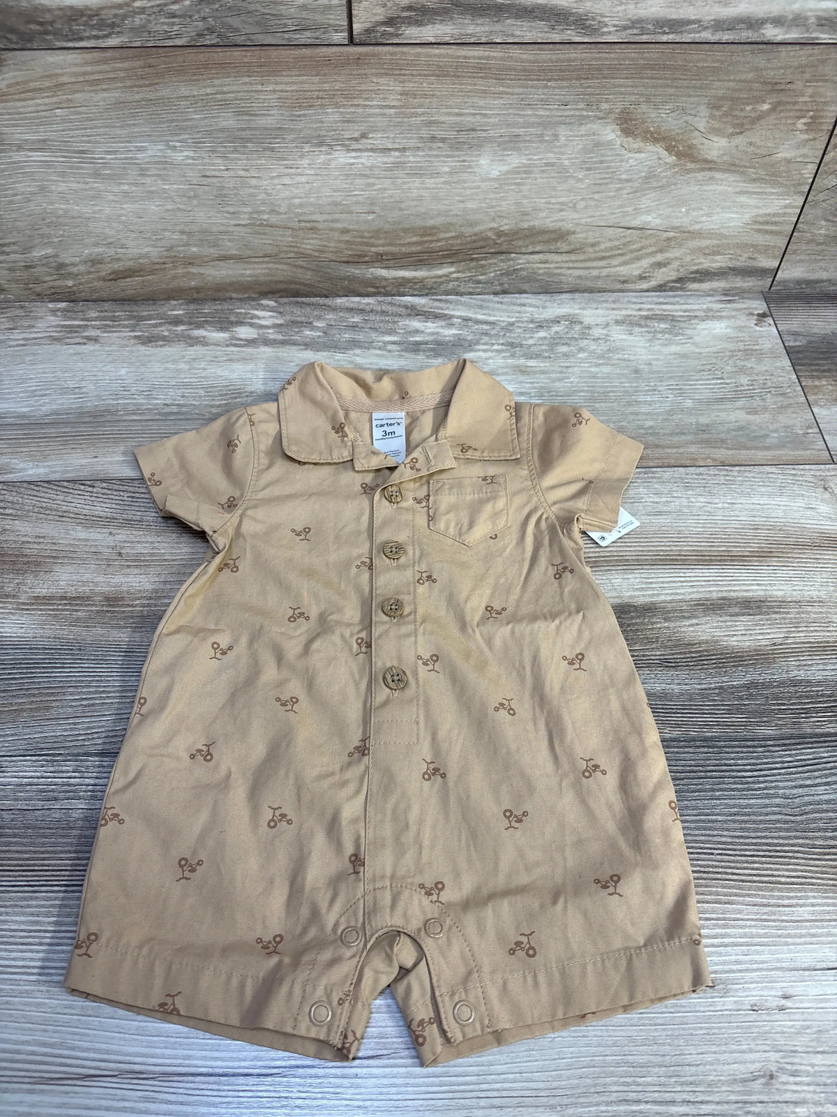 Front view of Carter’s tan polo romper in 3-month size showcasing bicycle pattern, collar, chest pocket, and snap closures
