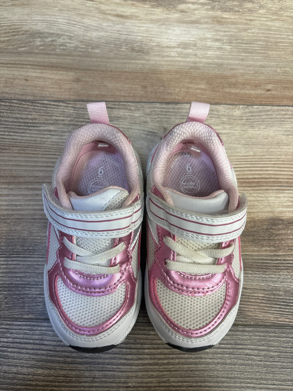 Pink and white toddler sneakers with velcro straps on wood floor