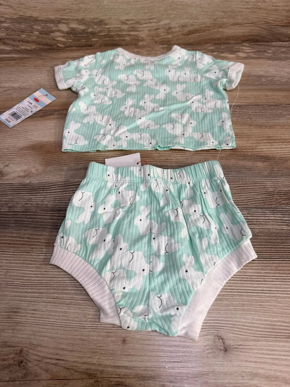 Flat lay of mint green baby two-piece shirt and shorts with white bunny print, ribbed texture and elastic waist on wood