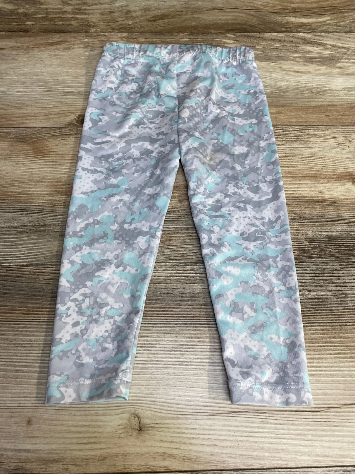 Flat-lay of Under Armour toddler leggings, grey and aqua camo, showing elastic waistband and full length on wood background