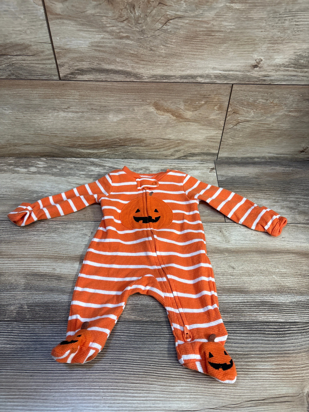Flat lay of newborn orange waffle-knit sleeper with white stripes and pumpkin appliqués on chest and feet on wood background