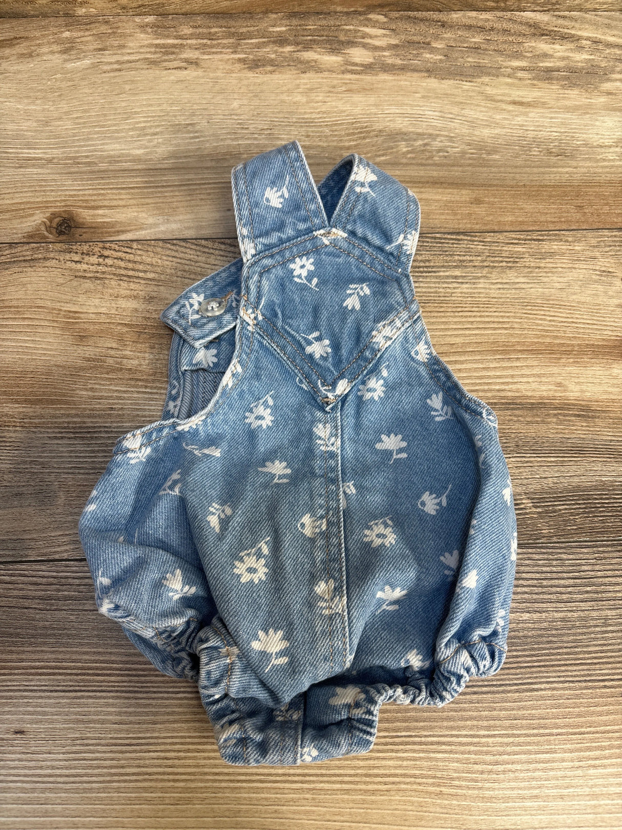 Baby denim romper with white floral print on wood background, gently used children’s clothing