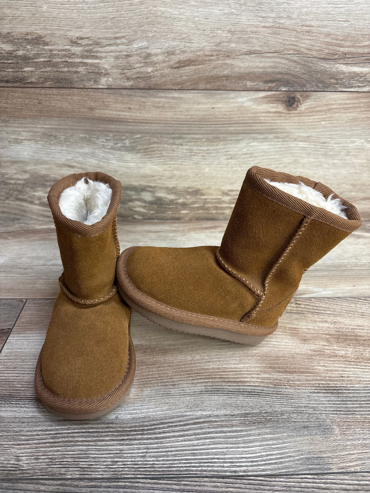 Pair of brown suede winter boots with white fleece lining on wooden floor