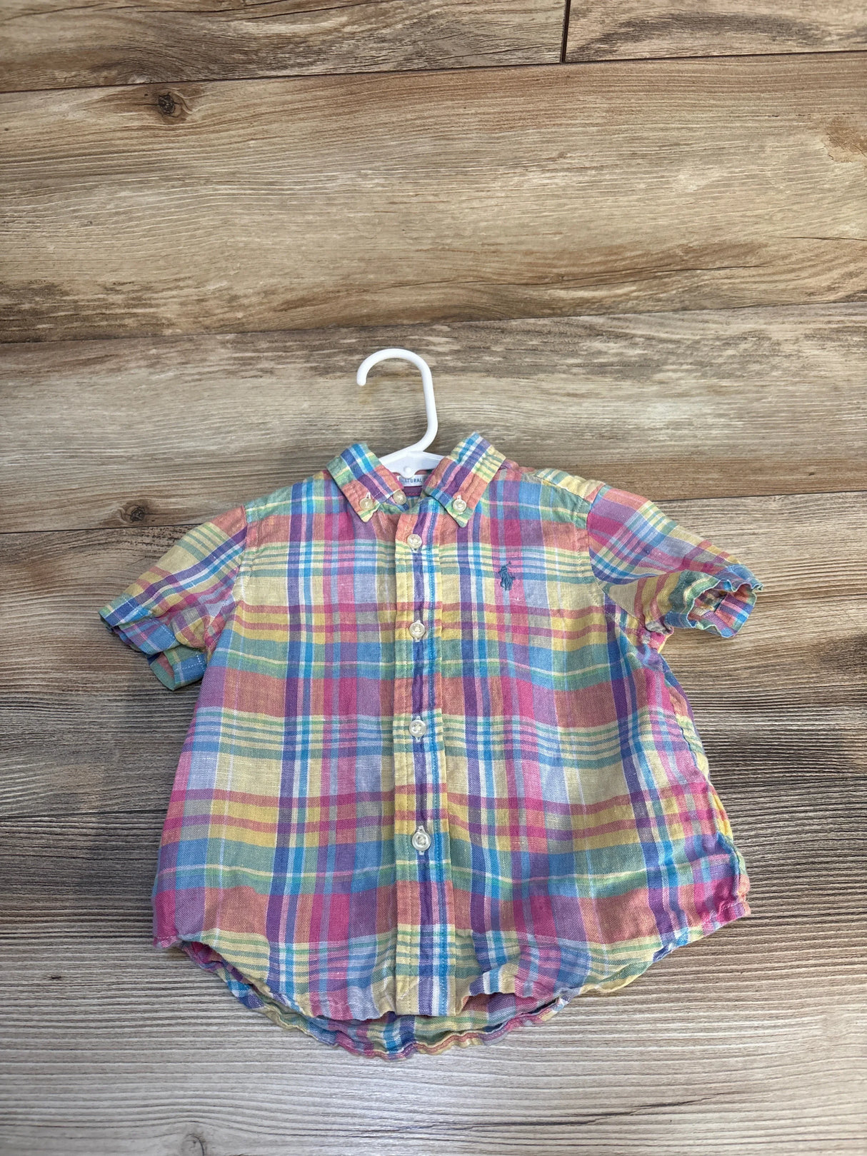 Colorful plaid short sleeve button-up toddler shirt on hanger, wood background