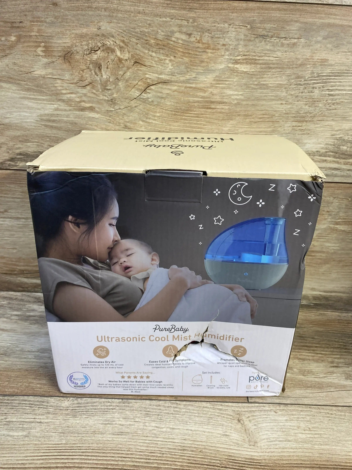 Front view of NEW PureBaby Ultrasonic Cool Mist Humidifier in original retail box showing mother and baby image on wood plank floor