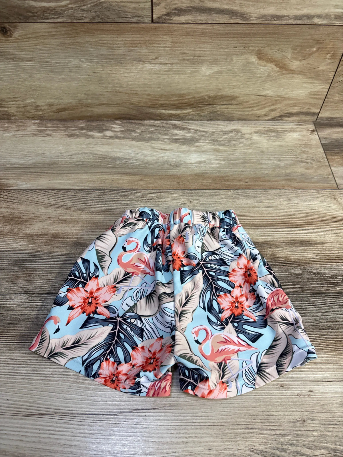 Flat view of blue Shein flamingo swim shorts showcasing a tropical floral print with a wood look background