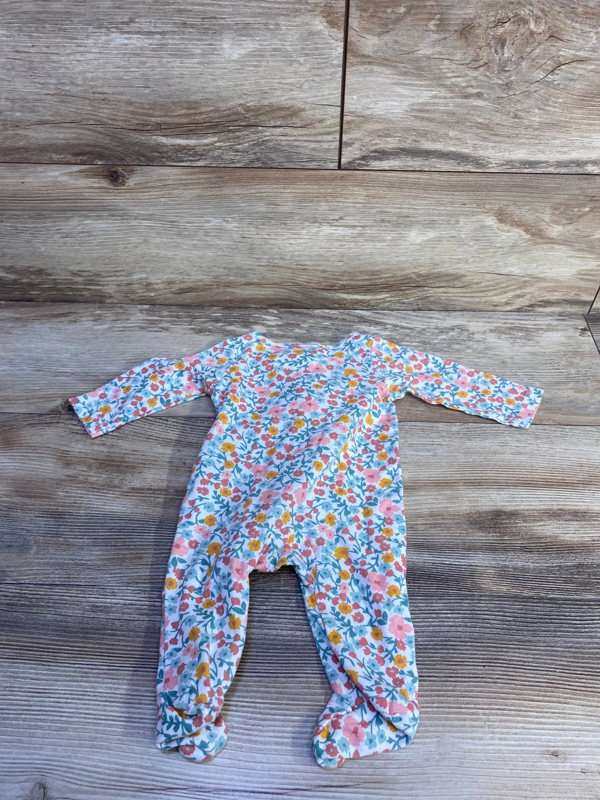 Flat lay of 3-month white floral baby sleeper with long sleeves and built-in footies on wood background