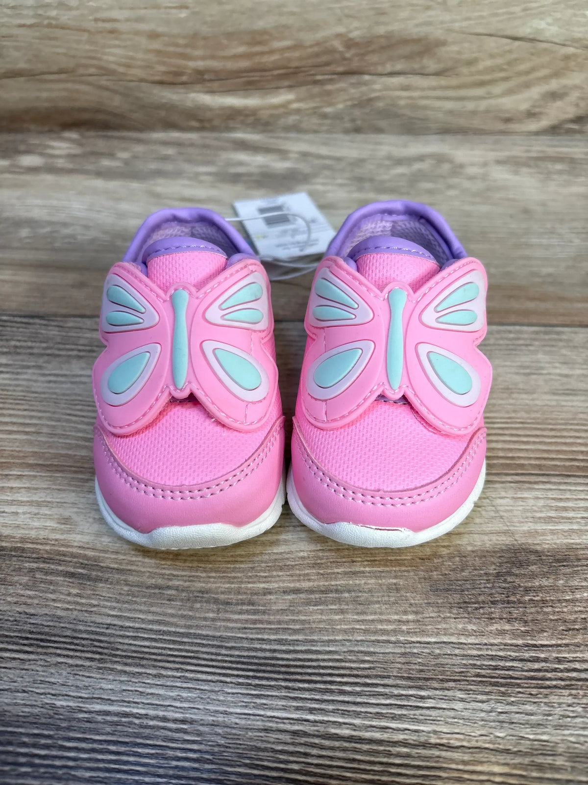 Front view of Just One You Butterfly sneakers, toddler size 3C, pink with butterfly wing appliques and soles on wooden floor