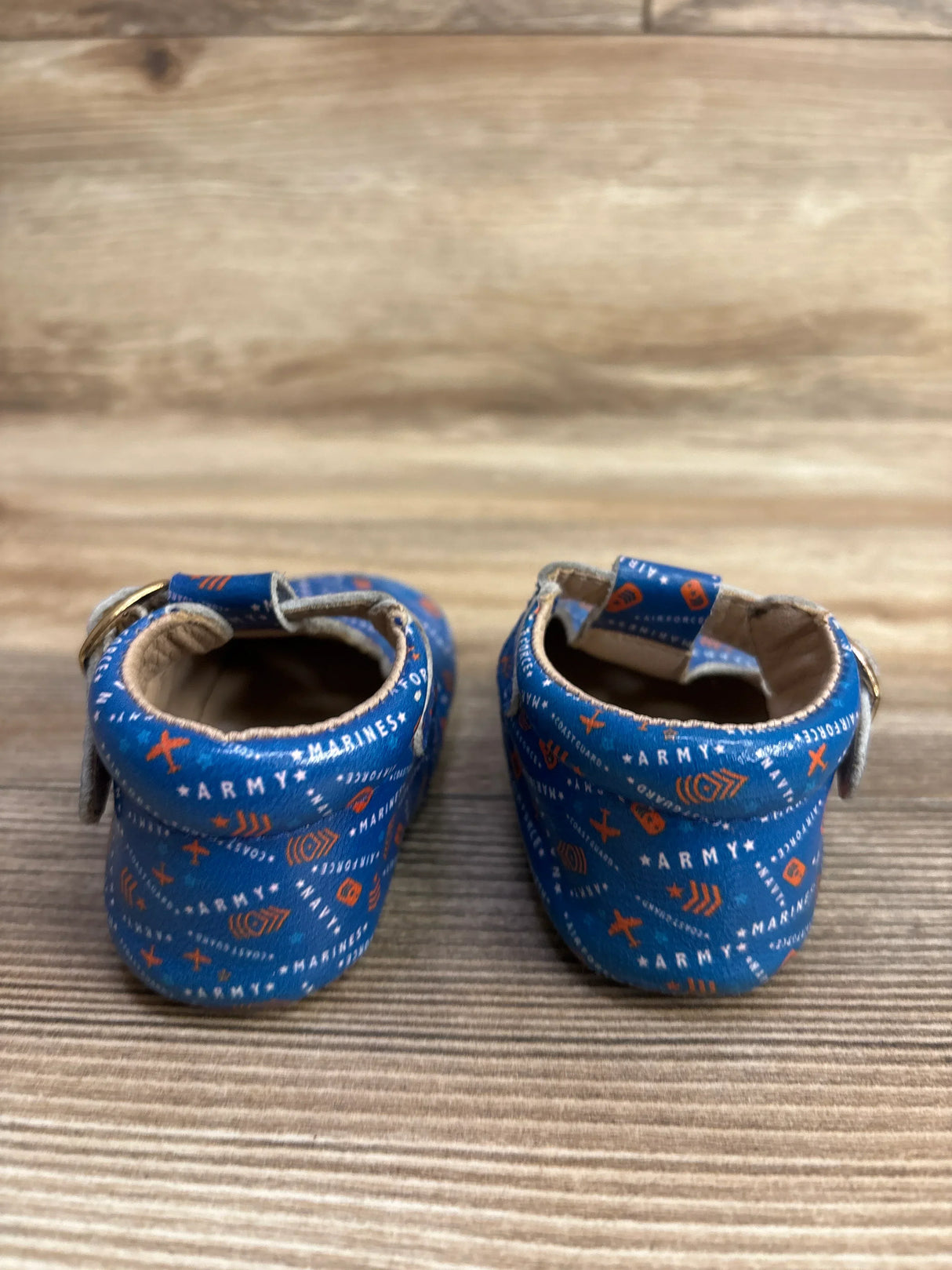 Blue baby shoes with military-themed print on wooden background