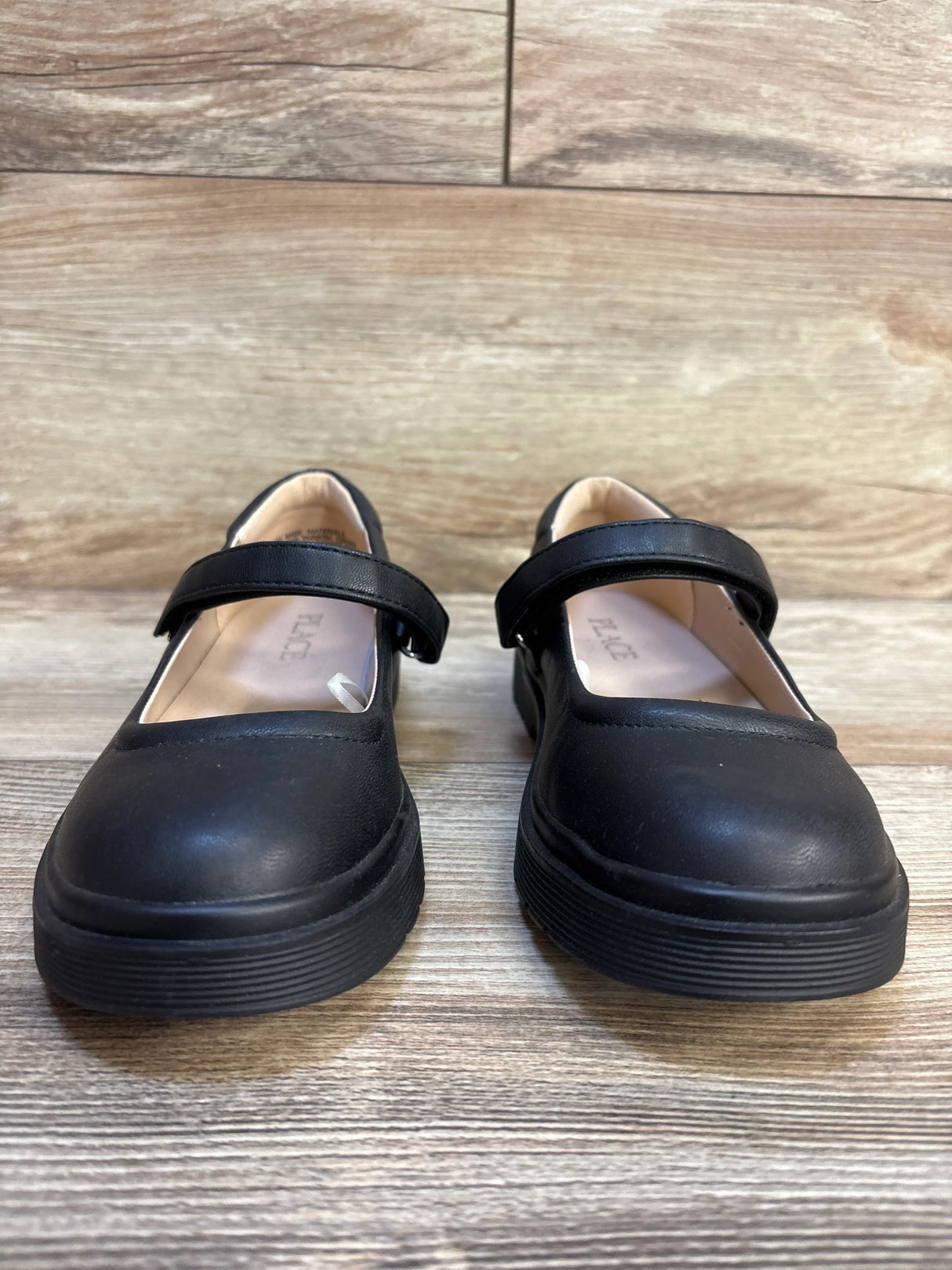 Black girls' Mary Jane dress shoes with strap, displayed on wooden floor