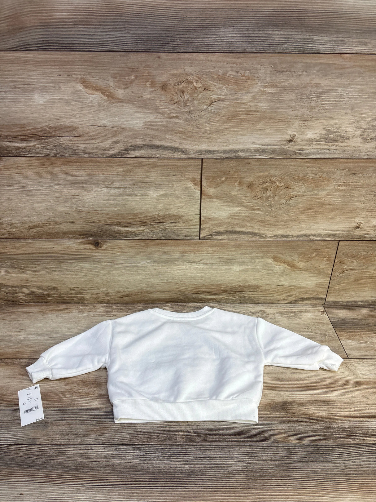Flat-lay back view of white Disney Junior Minnie Mouse bow sweatshirt with ribbed hem and tag on wood background
