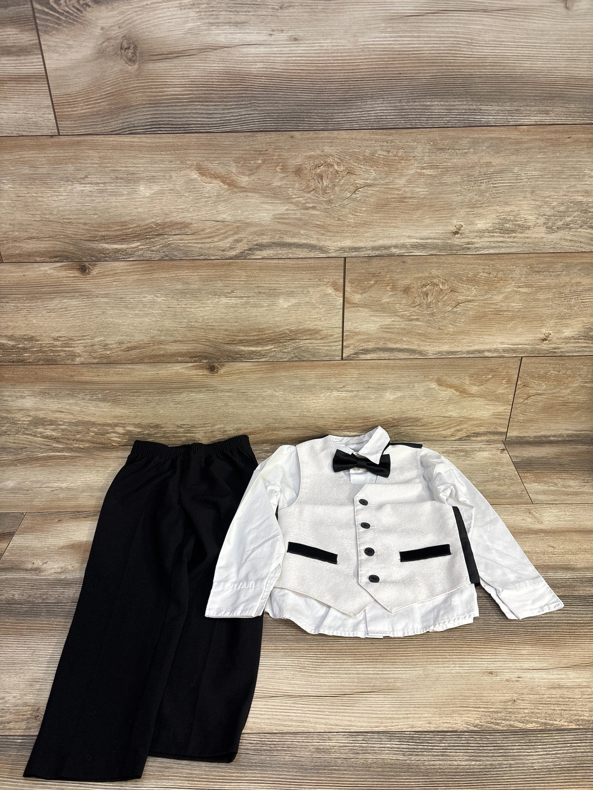 Children's formal outfit with black pants, white shirt, white vest, and black bow tie on wooden floor