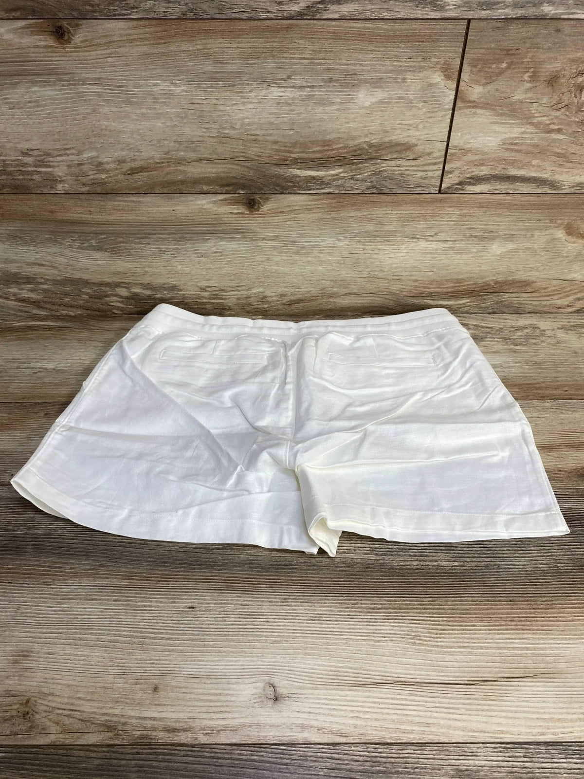 Flat-lay back view of Gap maternity linen cotton shorts, white, with elastic waistband and back pockets on wood background