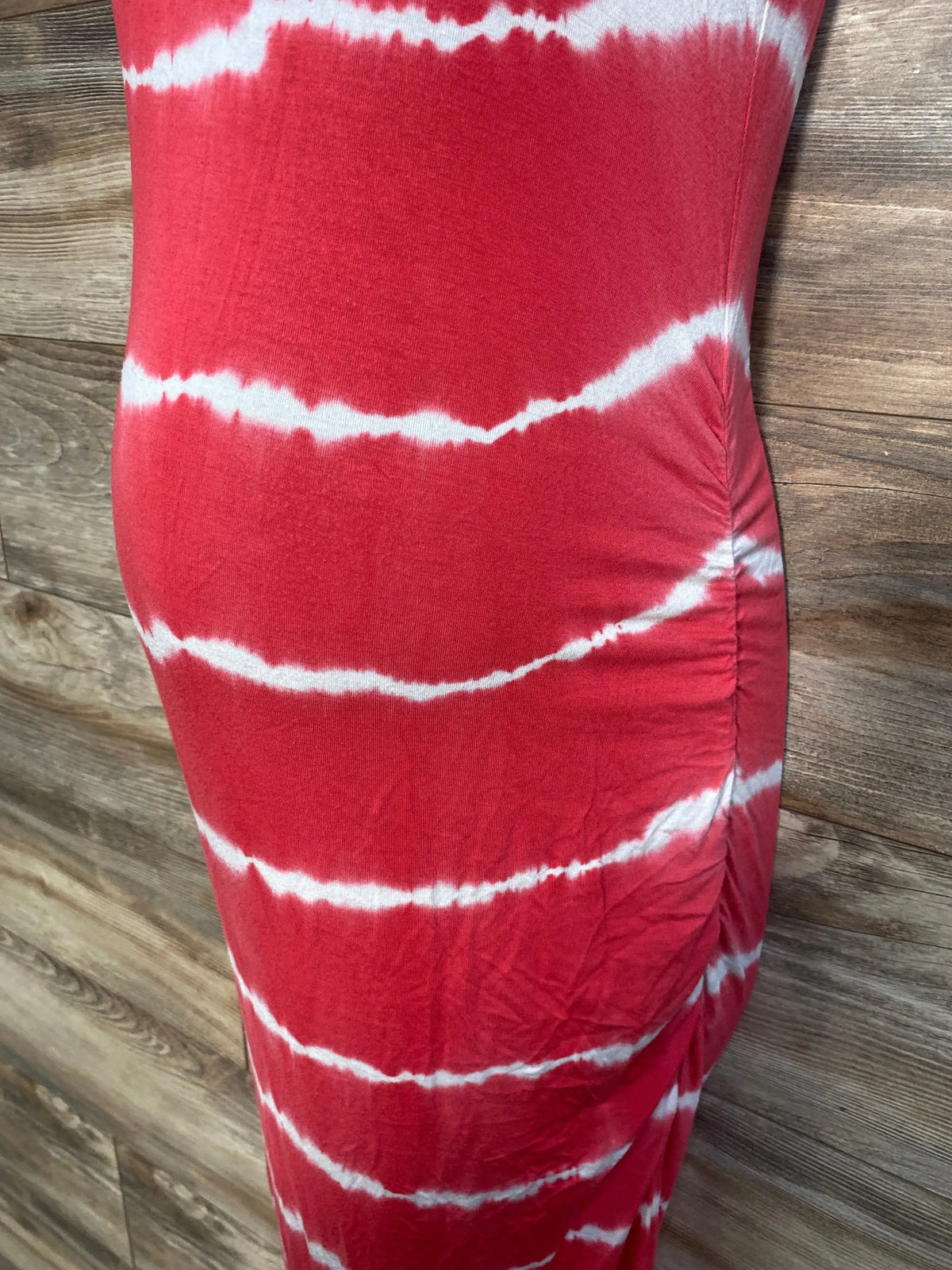 Side view of Isabel maternity bodycon mini dress in red tie-dye, showing ruched side seam and fitted silhouette on wood floor