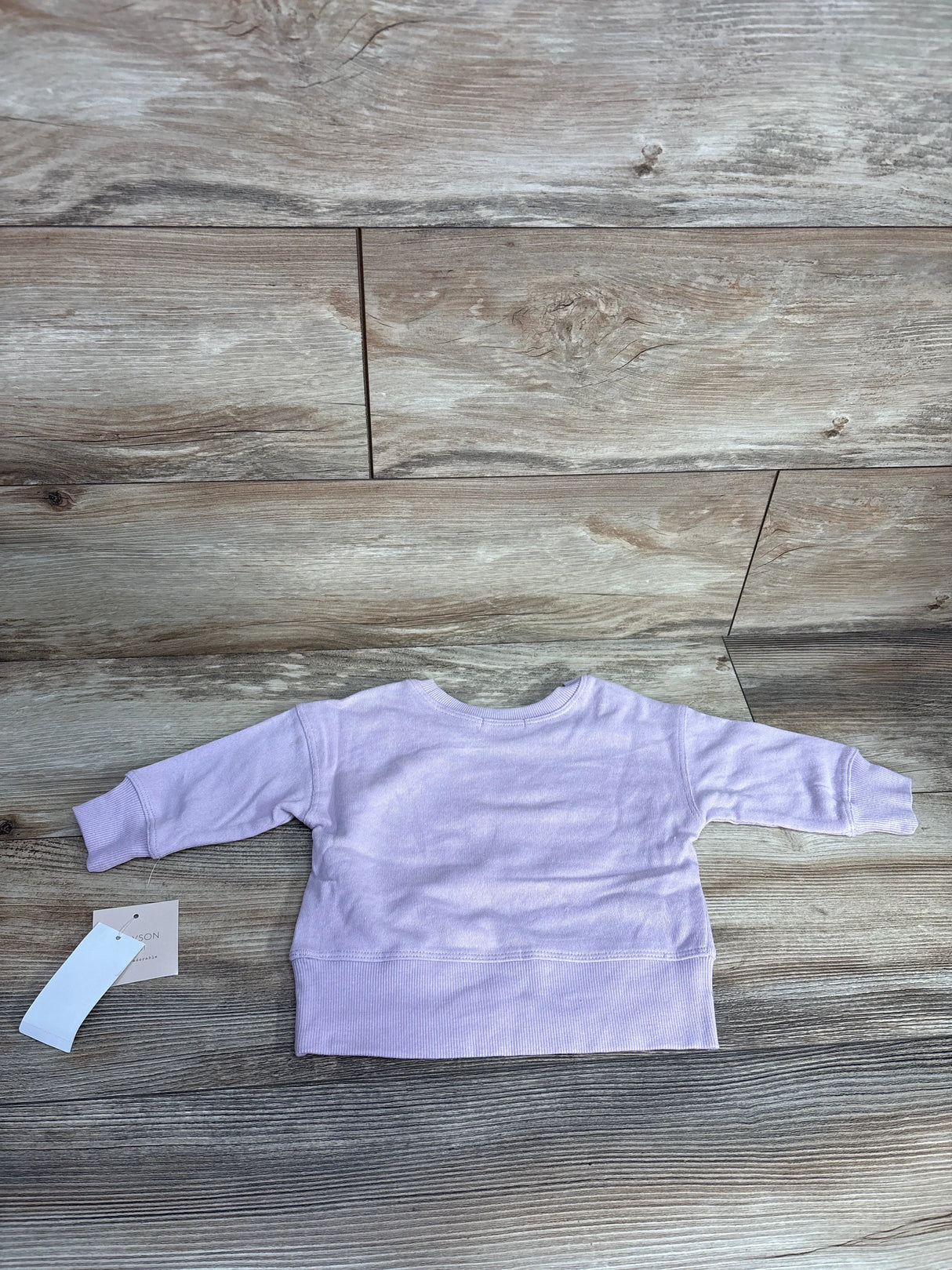 Back view of light purple toddler sweatshirt laid on wooden floor with attached tags