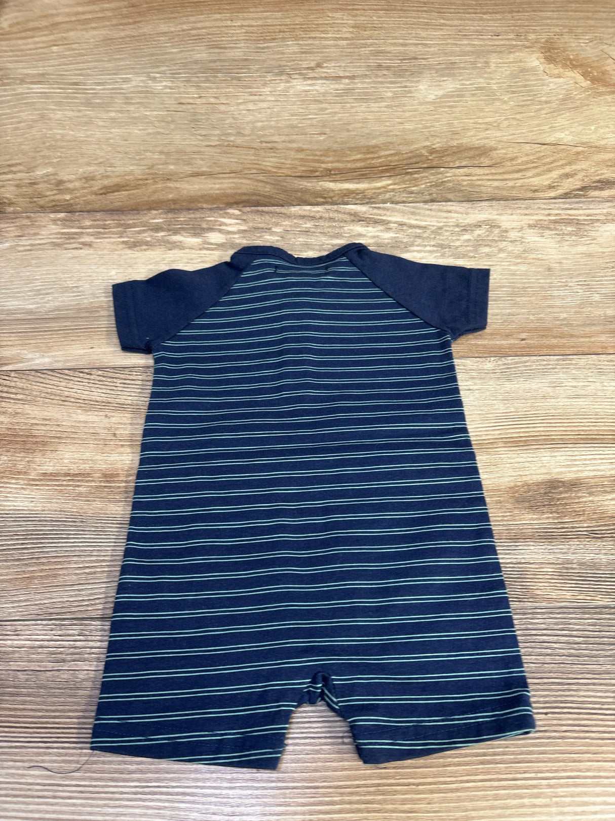 Flat lay of navy striped shortie romper showing raglan sleeves and horizontal light-blue stripes on wood floor