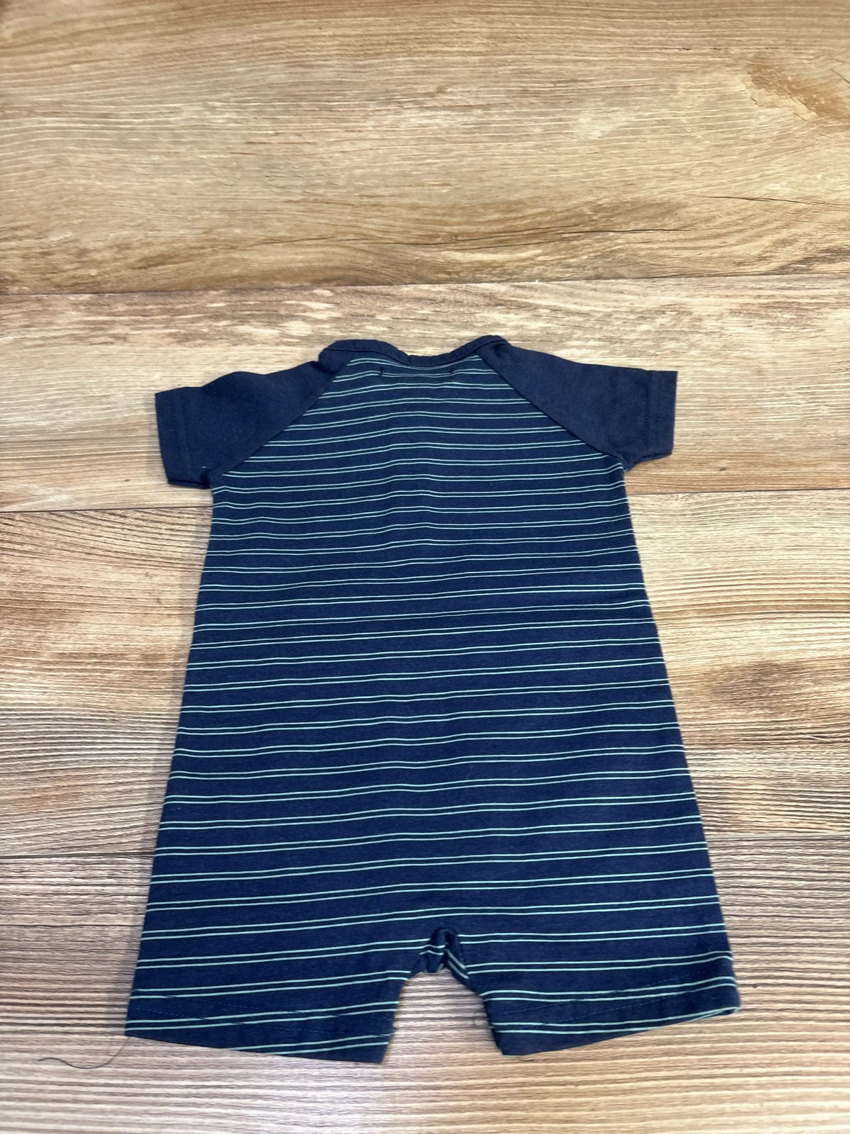 Flat lay of navy striped shortie romper showing raglan sleeves and horizontal light-blue stripes on wood floor