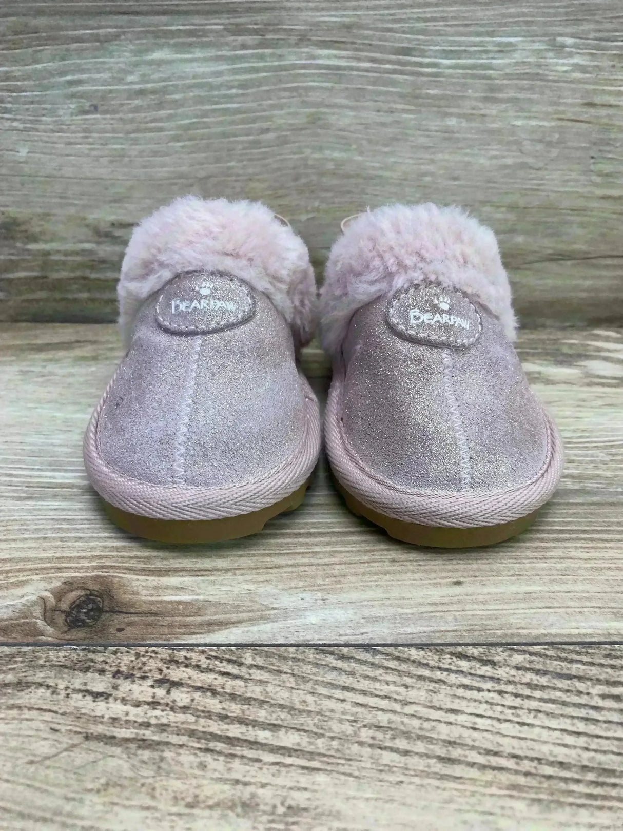 Front view of BEARPAW Rebecca suede slippers showcasing light pink suede and fluffy sheepskin cuff on wooden surface