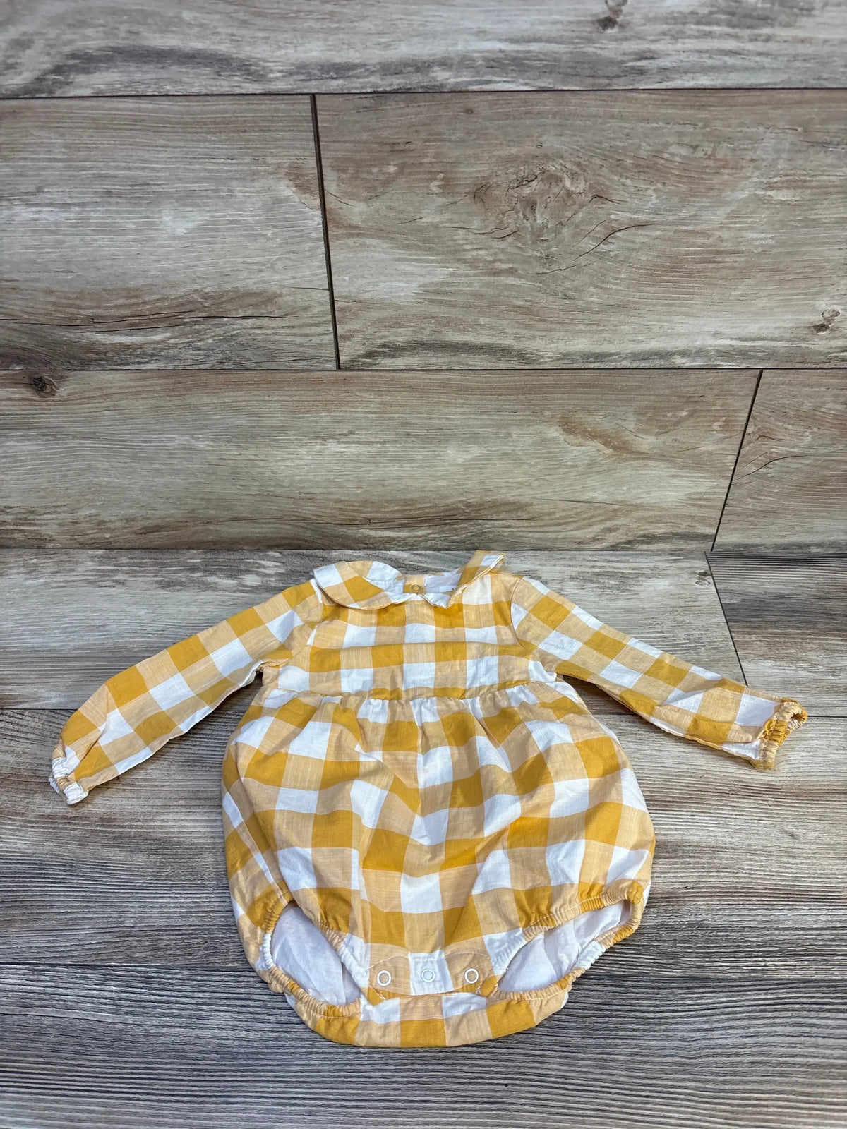 Yellow and white gingham baby romper with long sleeves, laid flat on wood floor