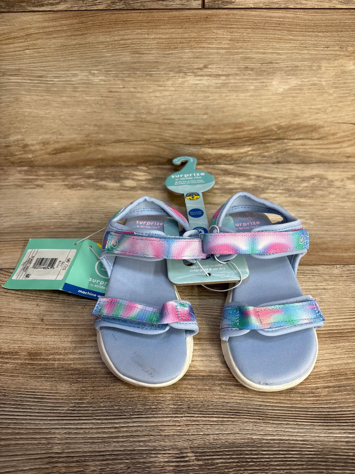 Top-down view of Surprize Lumos light-up toddler sandals size 11C showcasing pastel tie-dye straps and Velcro closures on wood background
