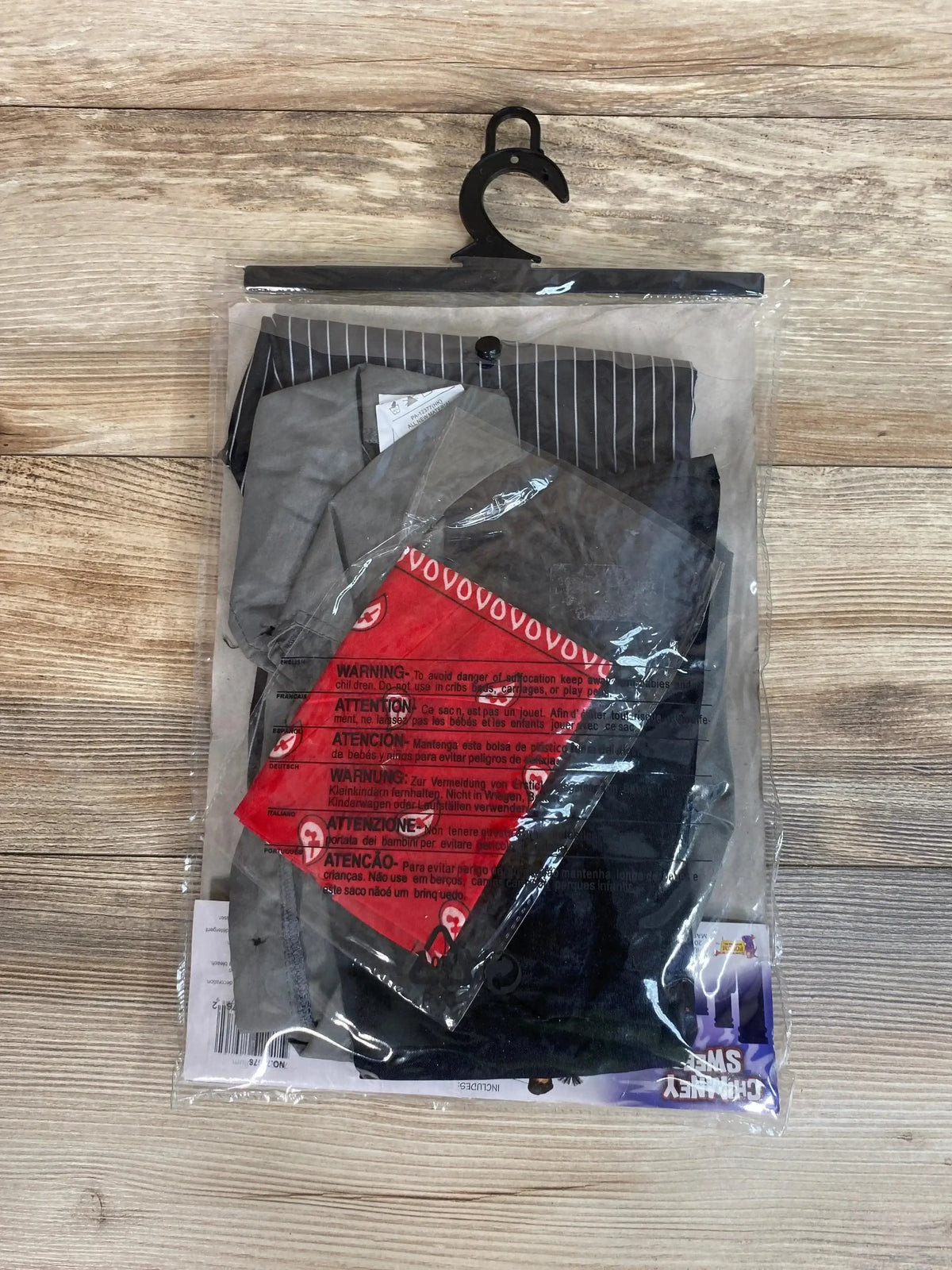 Top view of packaged chimney sweep toddler costume (4T-6) with grey jacket, black pants and red bandana on wood