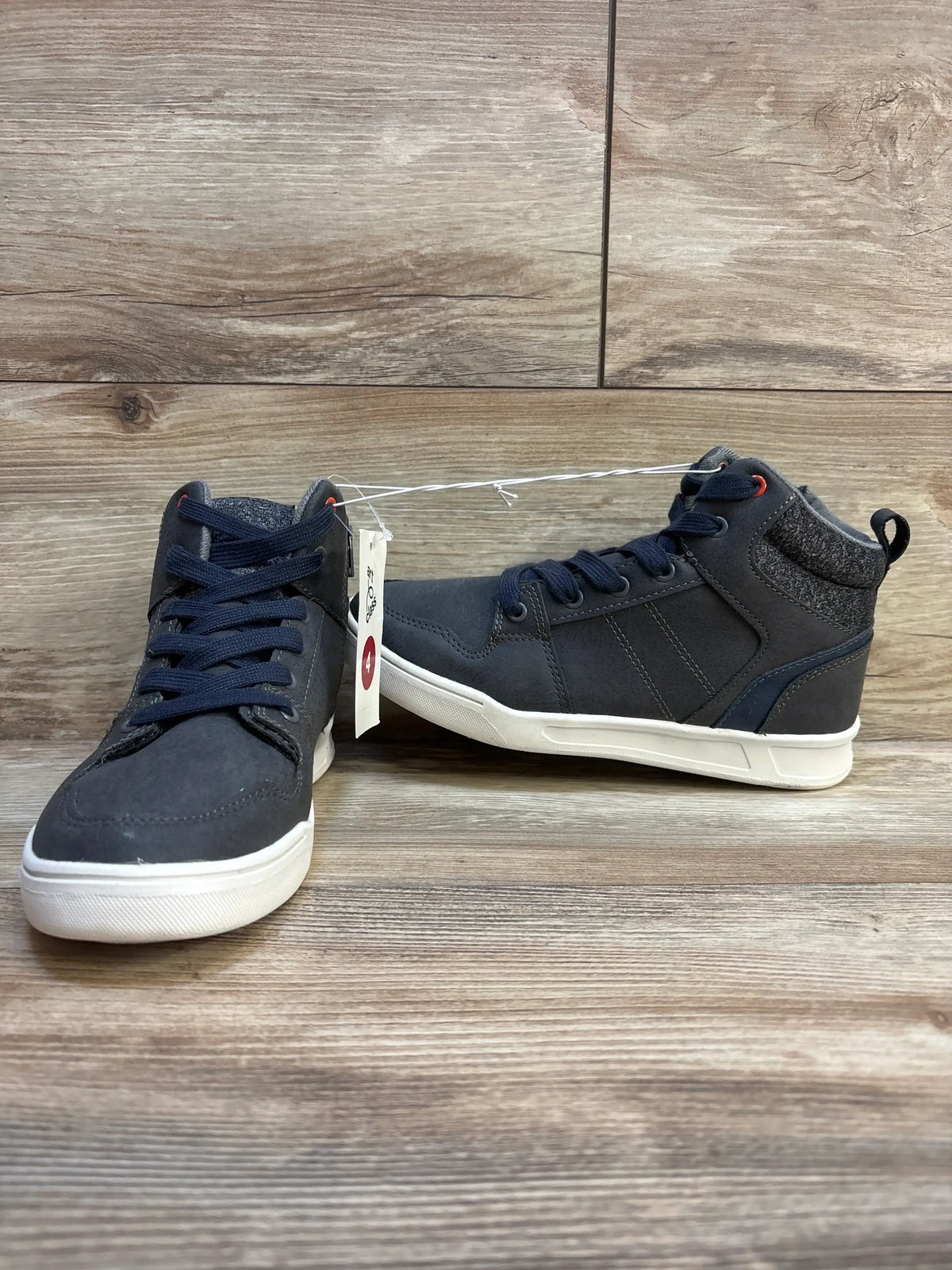 Pair of navy blue kids high top sneakers with white soles on wood floor