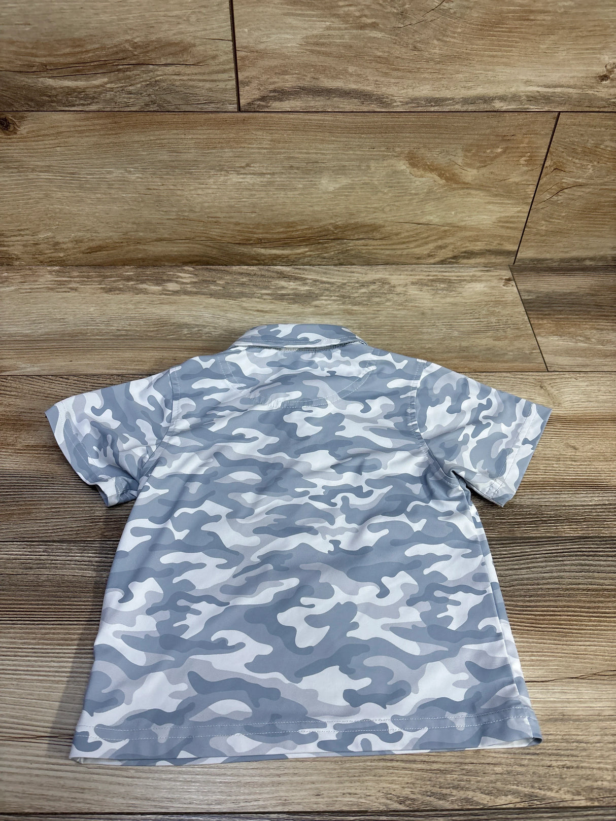 Back view of Clique Golf quick-dry camo polo shirt size 2T showcasing gray-white camouflage pattern and short sleeves, laid flat on wood background
