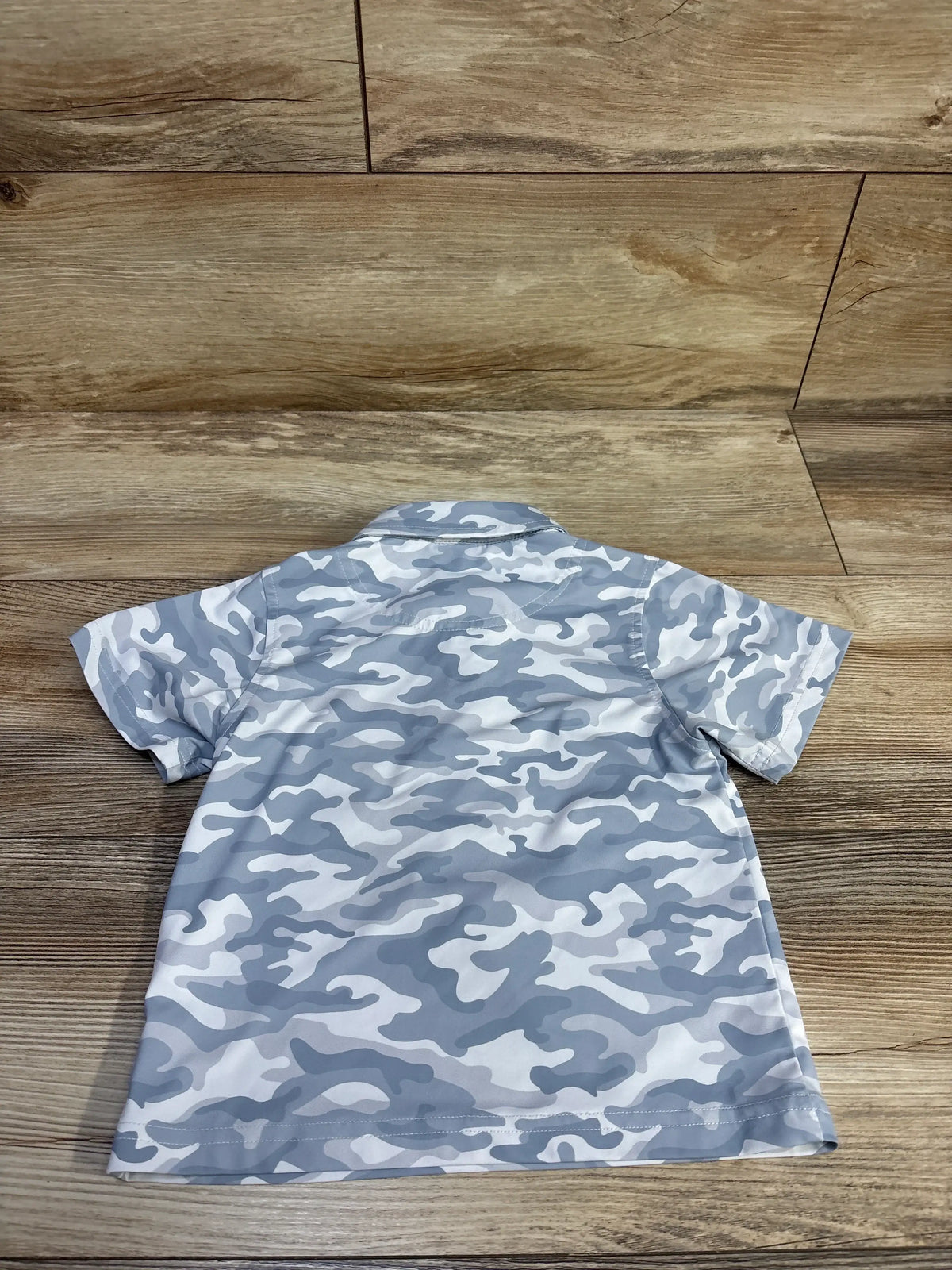 Back view of Clique Golf quick-dry camo polo shirt size 2T showcasing gray-white camouflage pattern and short sleeves, laid flat on wood background