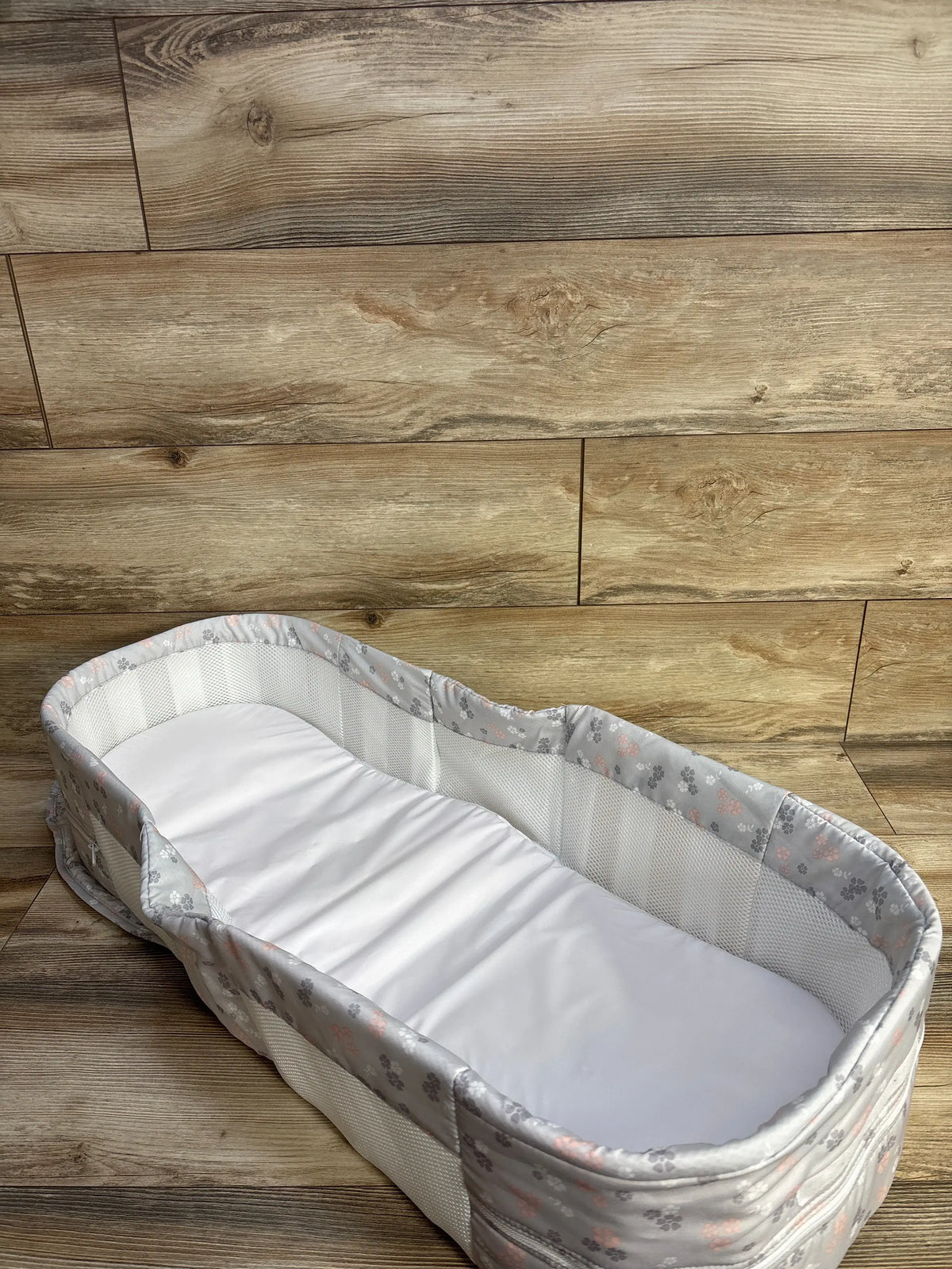 Angled top view of Baby Delight Snuggle Nest Harmony infant lounger with mesh sides and white padded insert on wood floor