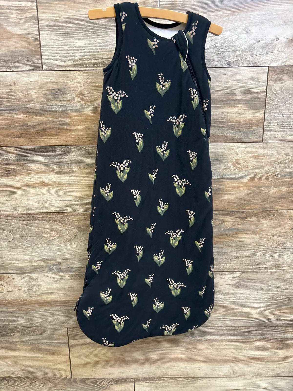 Front view of Kyte Baby 2.5 TOG bamboo sleep bag in black, size M, showcasing floral print and J-shaped double zipper with wood floor background