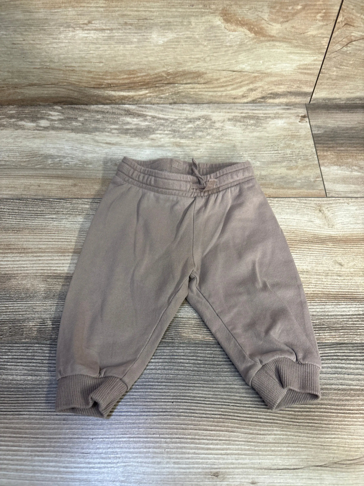 Flat lay of brown baby joggers size 3 months showing elastic drawstring waist and cuffed ankles on wood floor