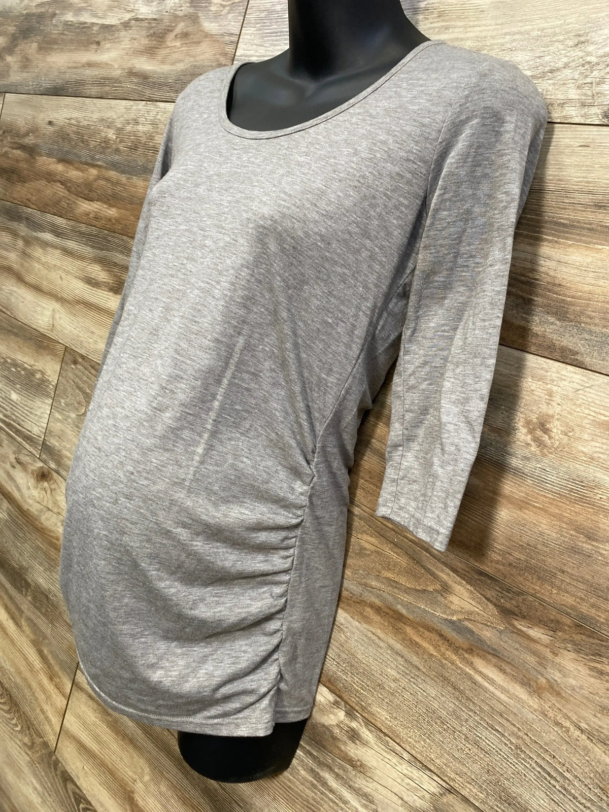 Front view of gray 3/4 sleeve ruched shirt in size small showcasing side ruching with a black mannequin on a wood plank background