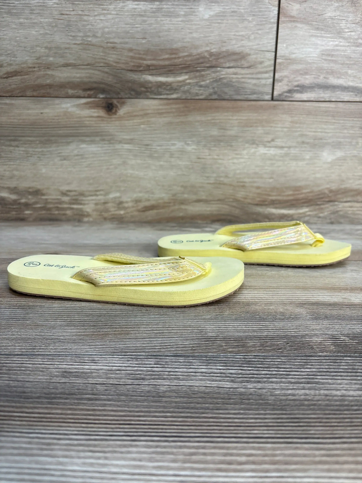 Yellow kids flip-flops with iridescent straps on wood background, children's footwear