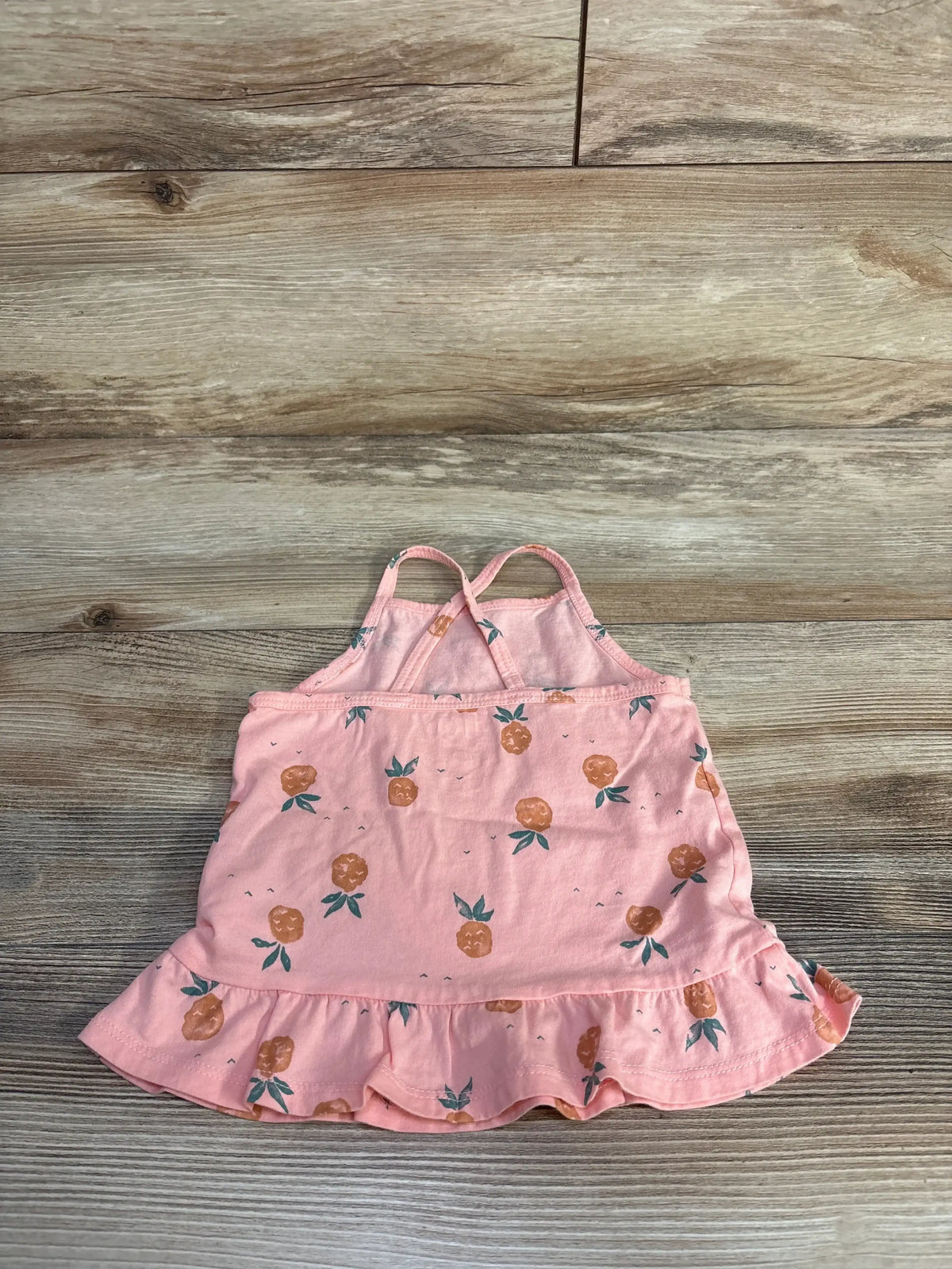 Flat lay of pink OshKosh 24-month tank top with pineapple print, ruffle hem, and crossed straps on light wood background